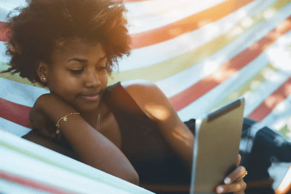 A person sitting in a hammock looking at a tablet Description automatically generated
